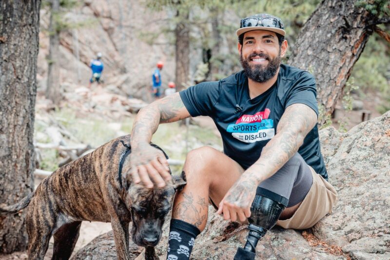 Cris, an NSCD participant and volunteer, sitting at the base of a climb with his dog